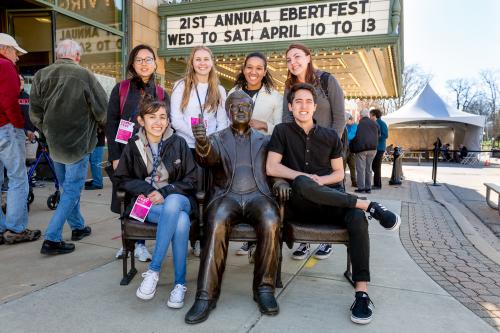 Young adults posing for a photo with the statue of Roger Ebert
